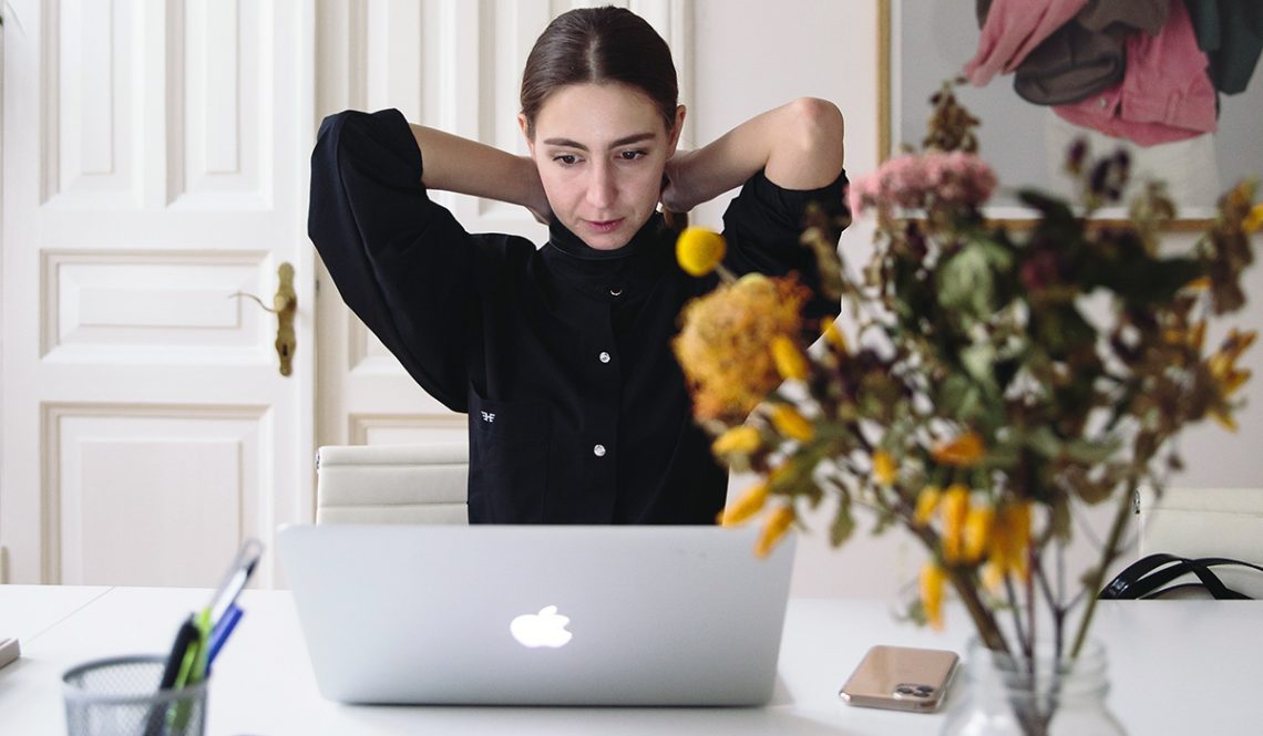Female sitting at desk in front of laptop with arms raised behind neck